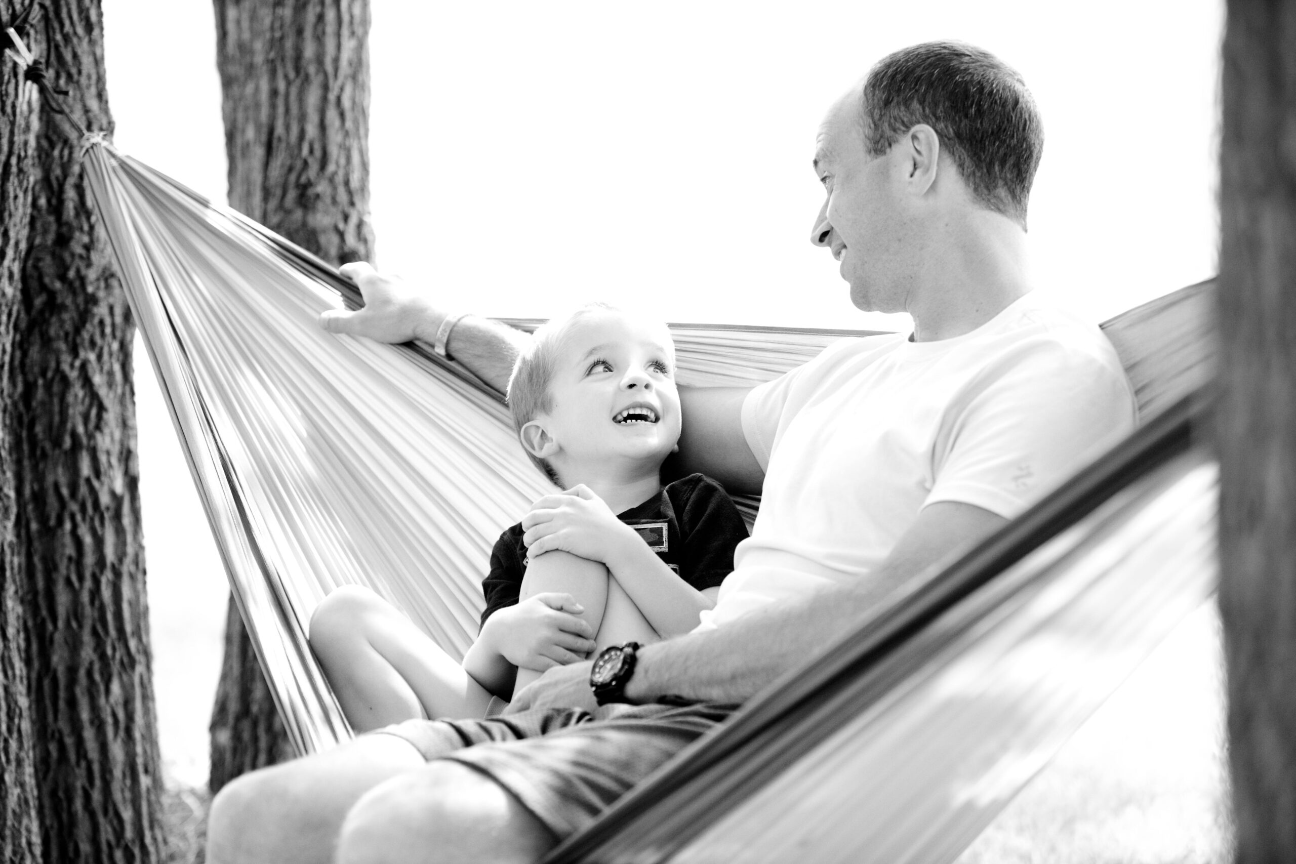 A parent looks at his son while sitting in a hammock.
